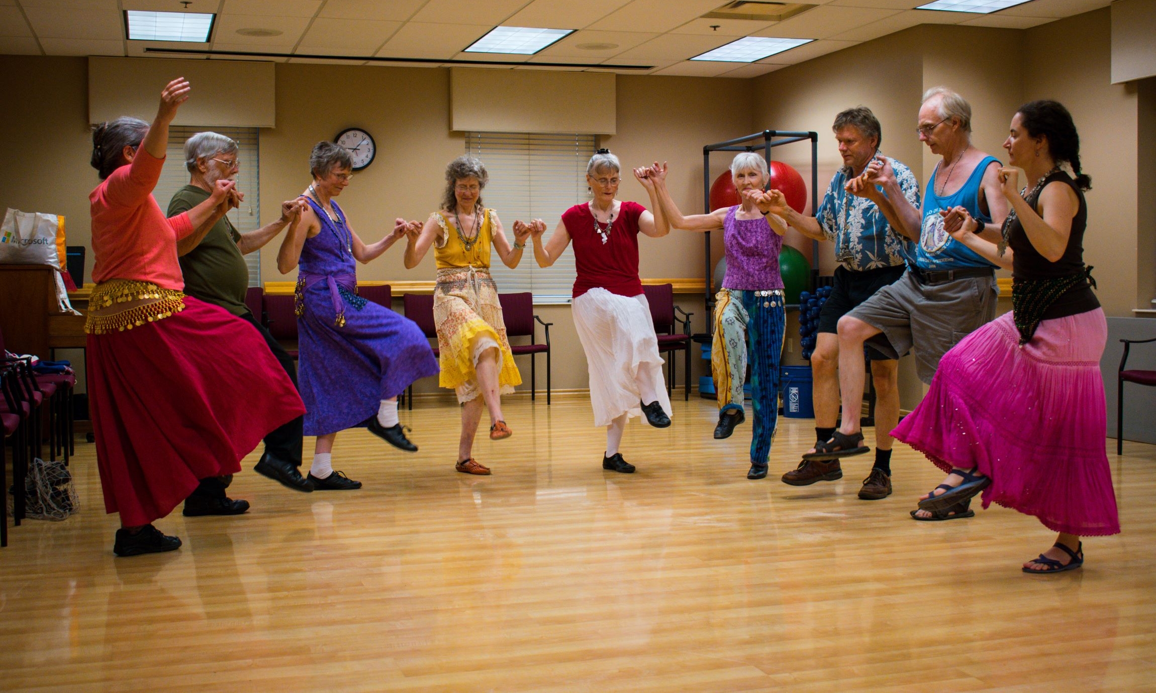 A group of people in a semi circle, holding hands and dancing by kicking up their legs