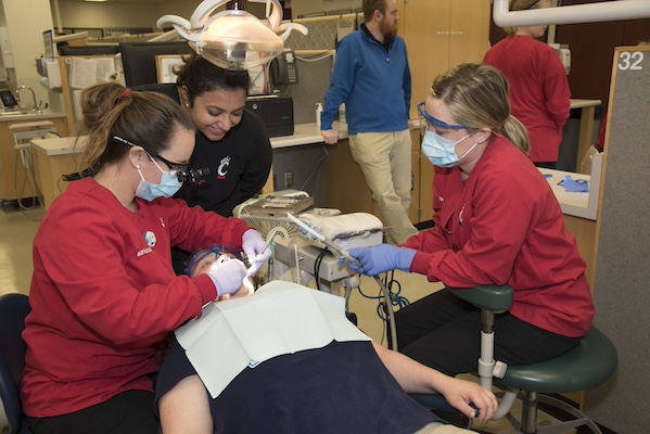 three students and a person sitting in a chair getting their teeth checked